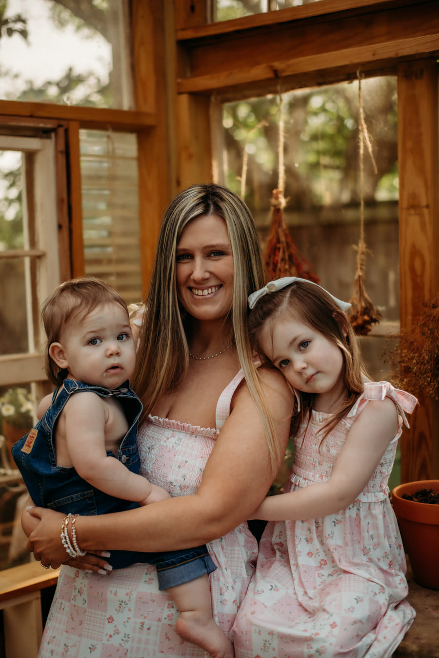 Kearstin Zumwalt standing in a greenhouse, holding her two young children.
